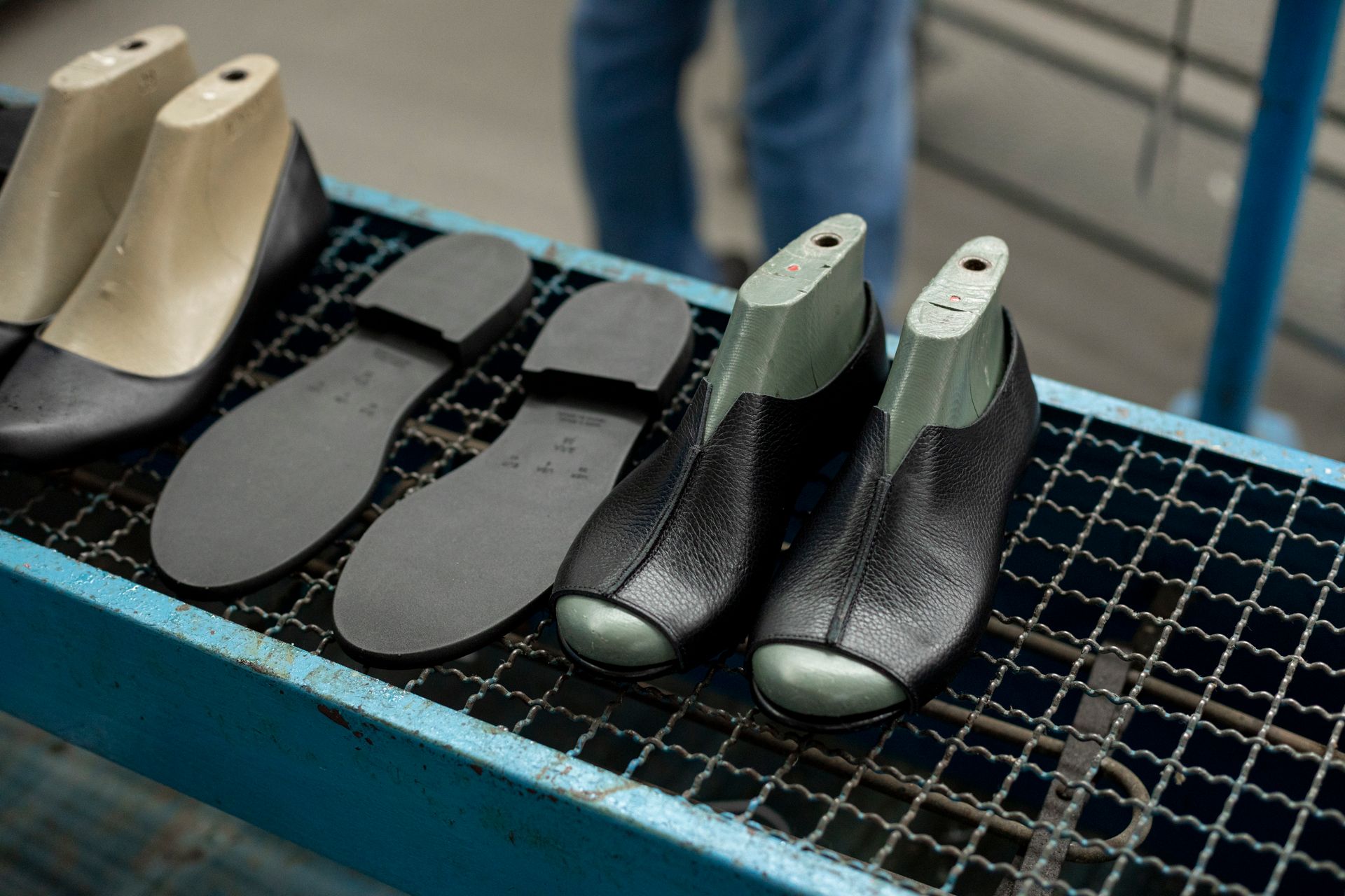 Hormas de zapato junto a plantillas y capelladas de cuero negro sobre una rejilla del taller