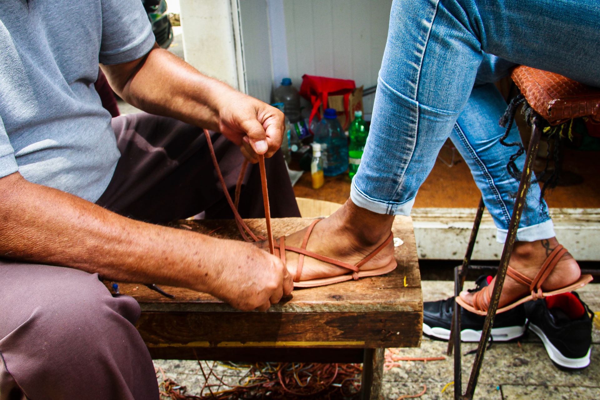 Manos de un artesano ajustando las tiras de cuero de una sandalia sobre el pie de una clienta