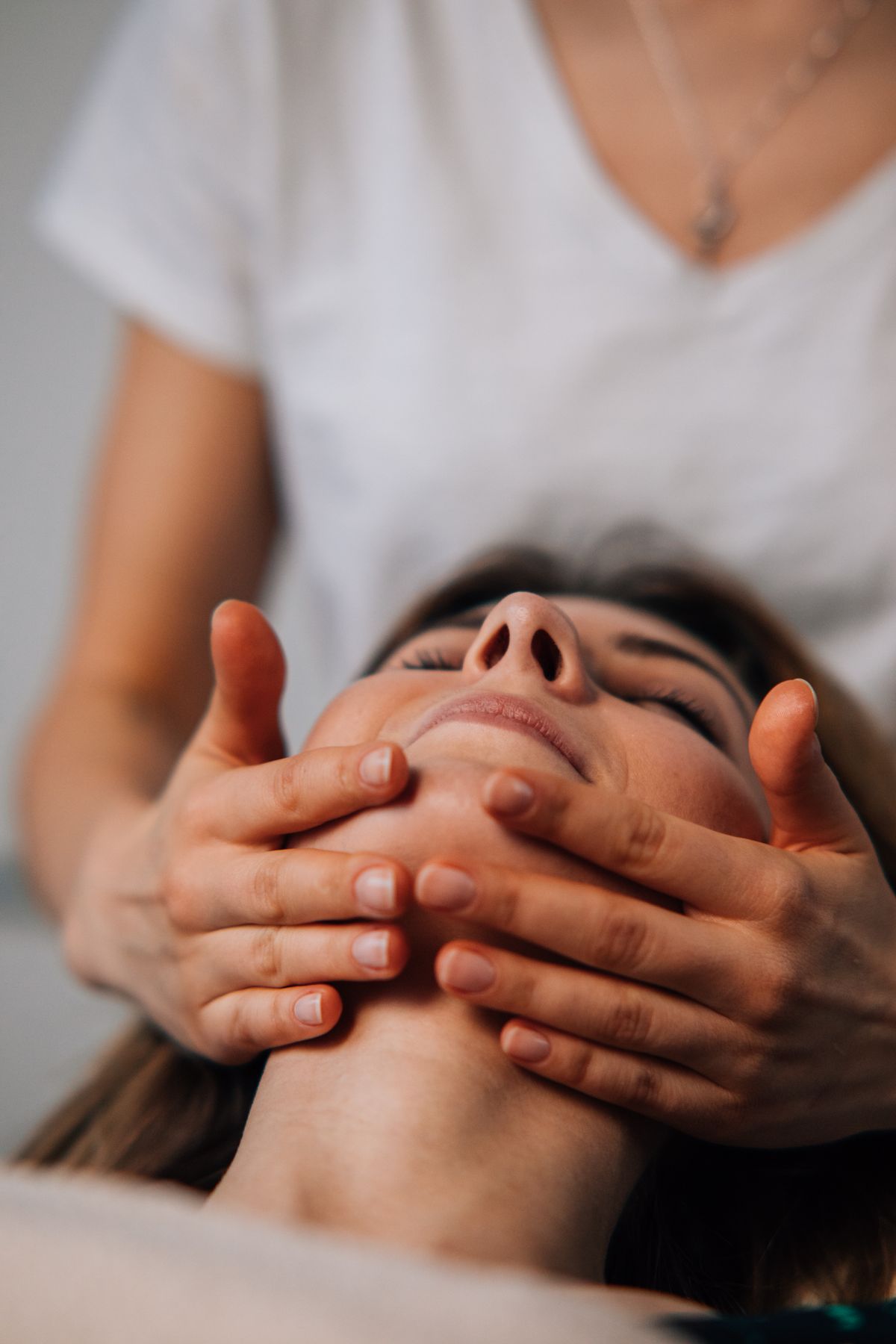 Manos de una cosmiatra que sostienen el rostro de una clienta con los ojos cerrados