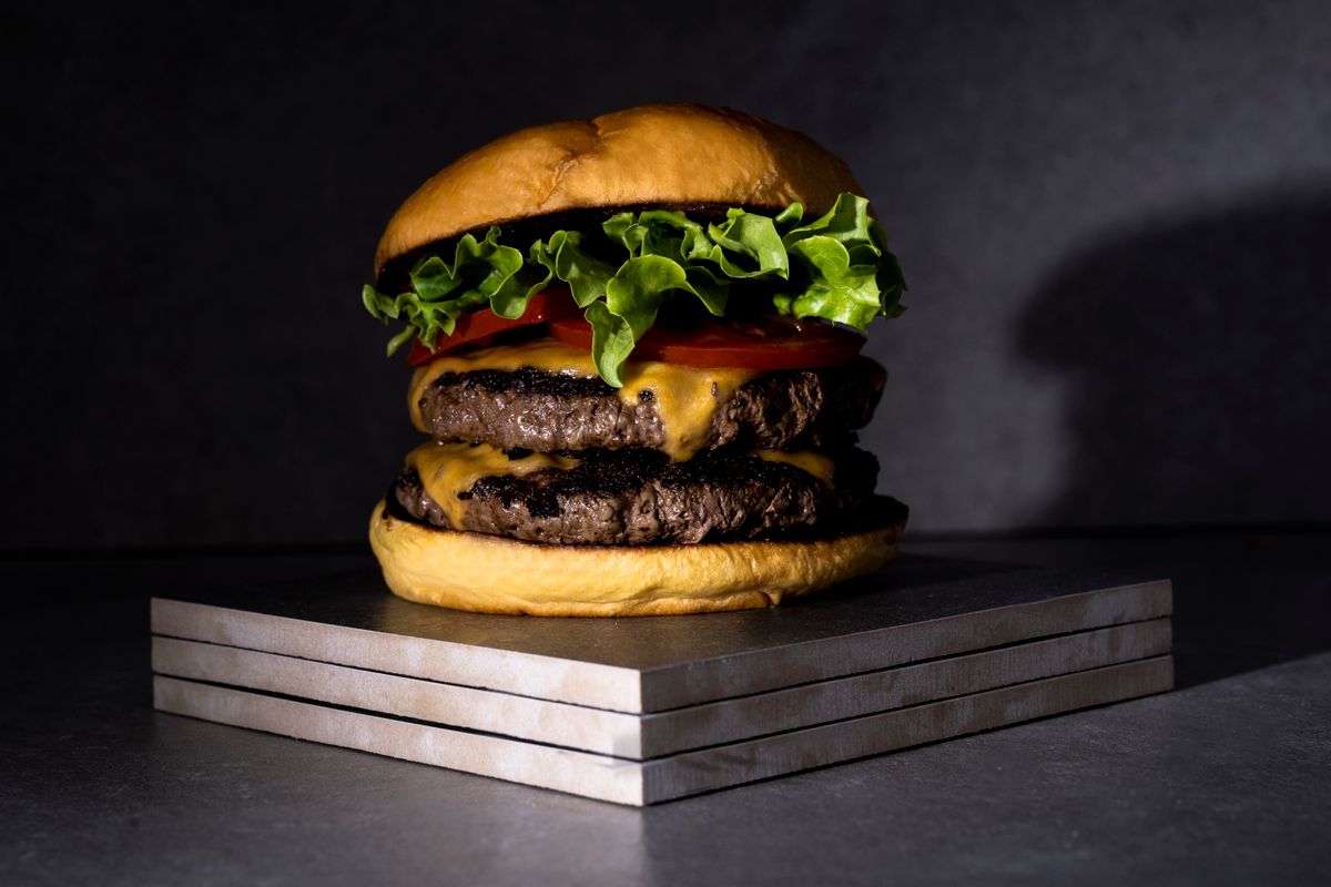 La Clásica: dos carnes con cheddar, tomate y lechuga, sobre bandejas de acero