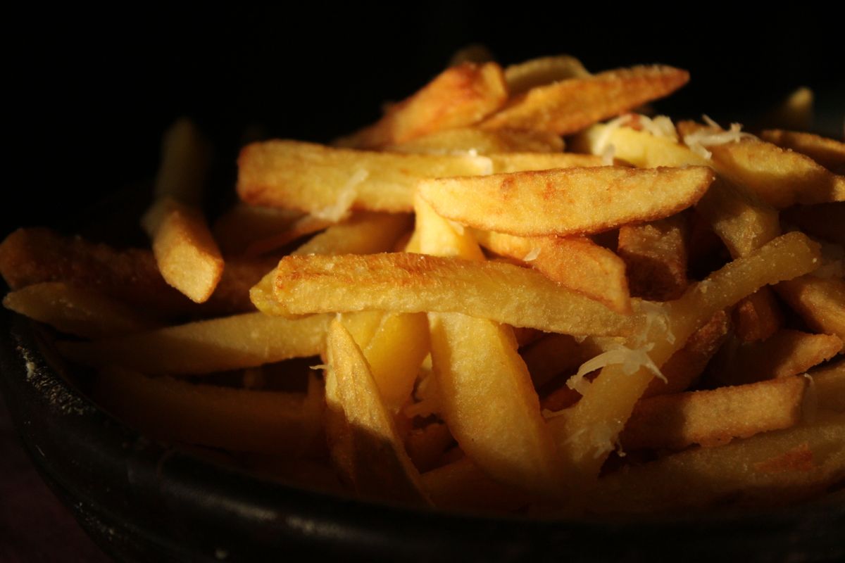 Papas fritas gruesas con queso rallado, sobre fondo oscuro