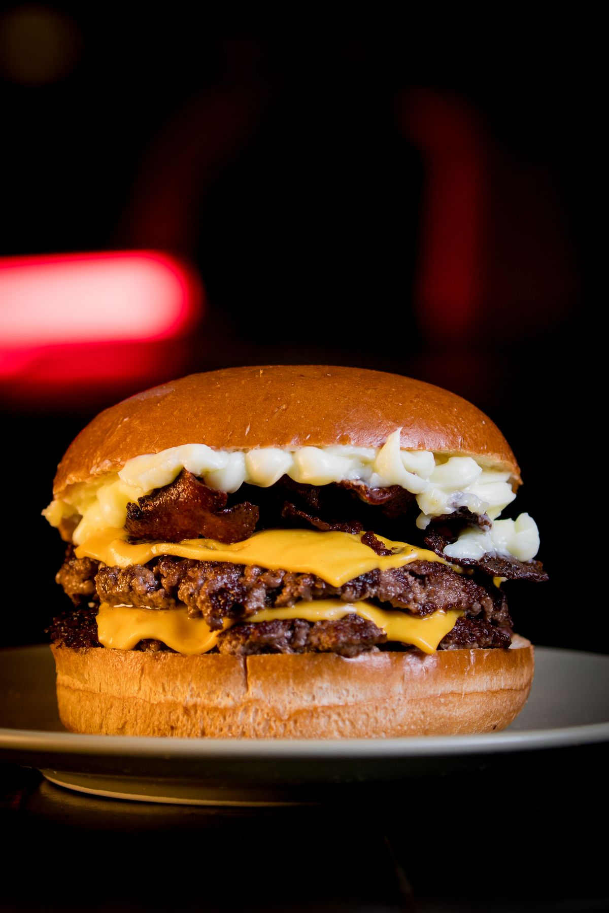 La Tocinera: dos carnes con cheddar, tocino y salsa blanca, con una luz roja de fondo