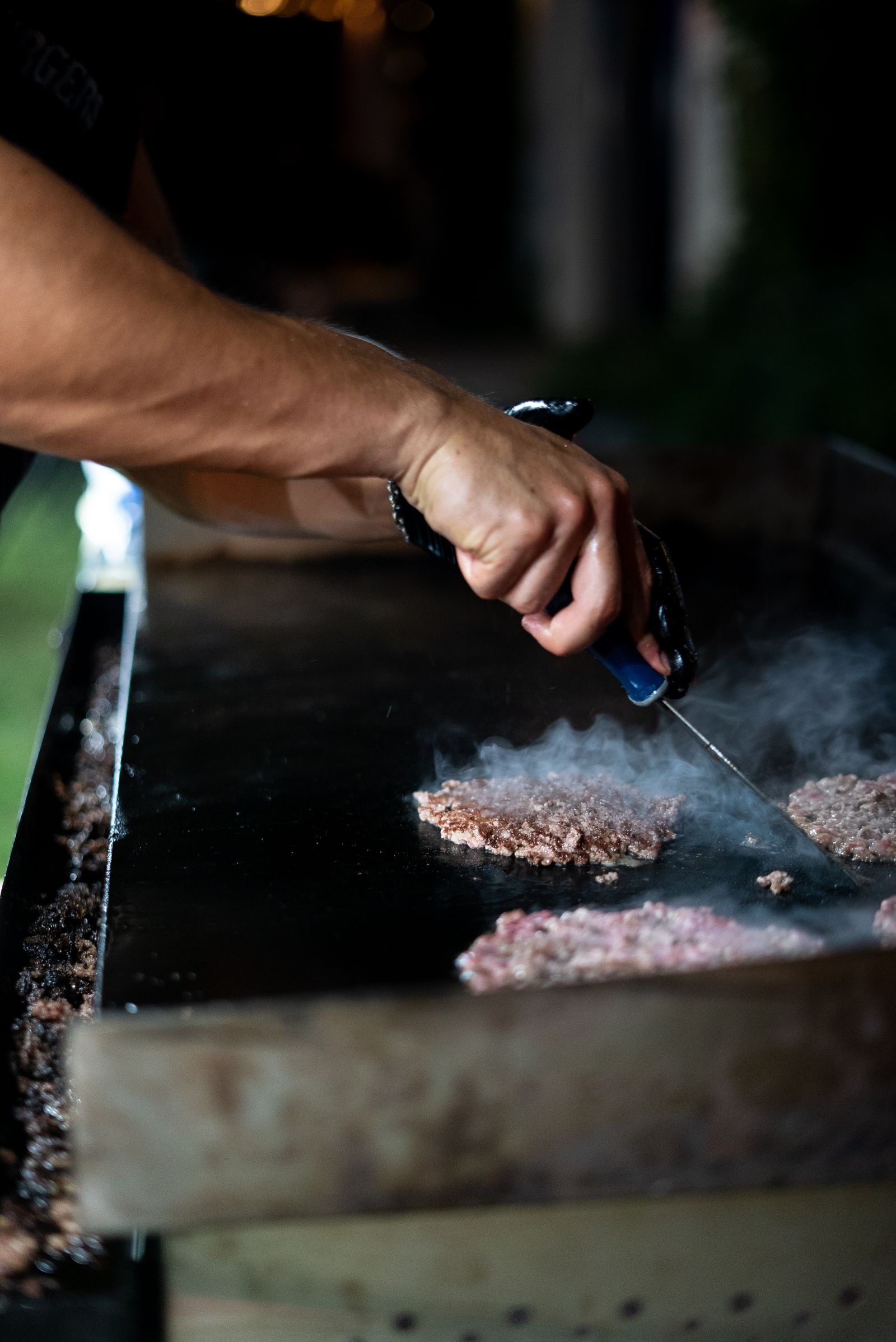 Una mano con espátula aplasta carnes sobre la plancha, de noche