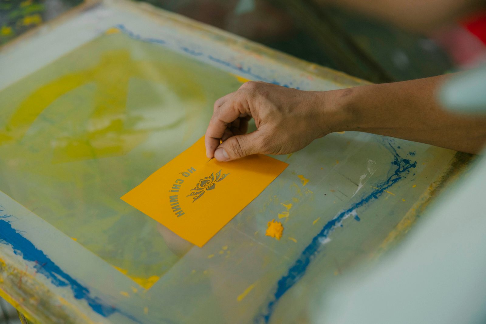 Una mano coloca una prueba impresa en amarillo sobre la malla manchada de tinta