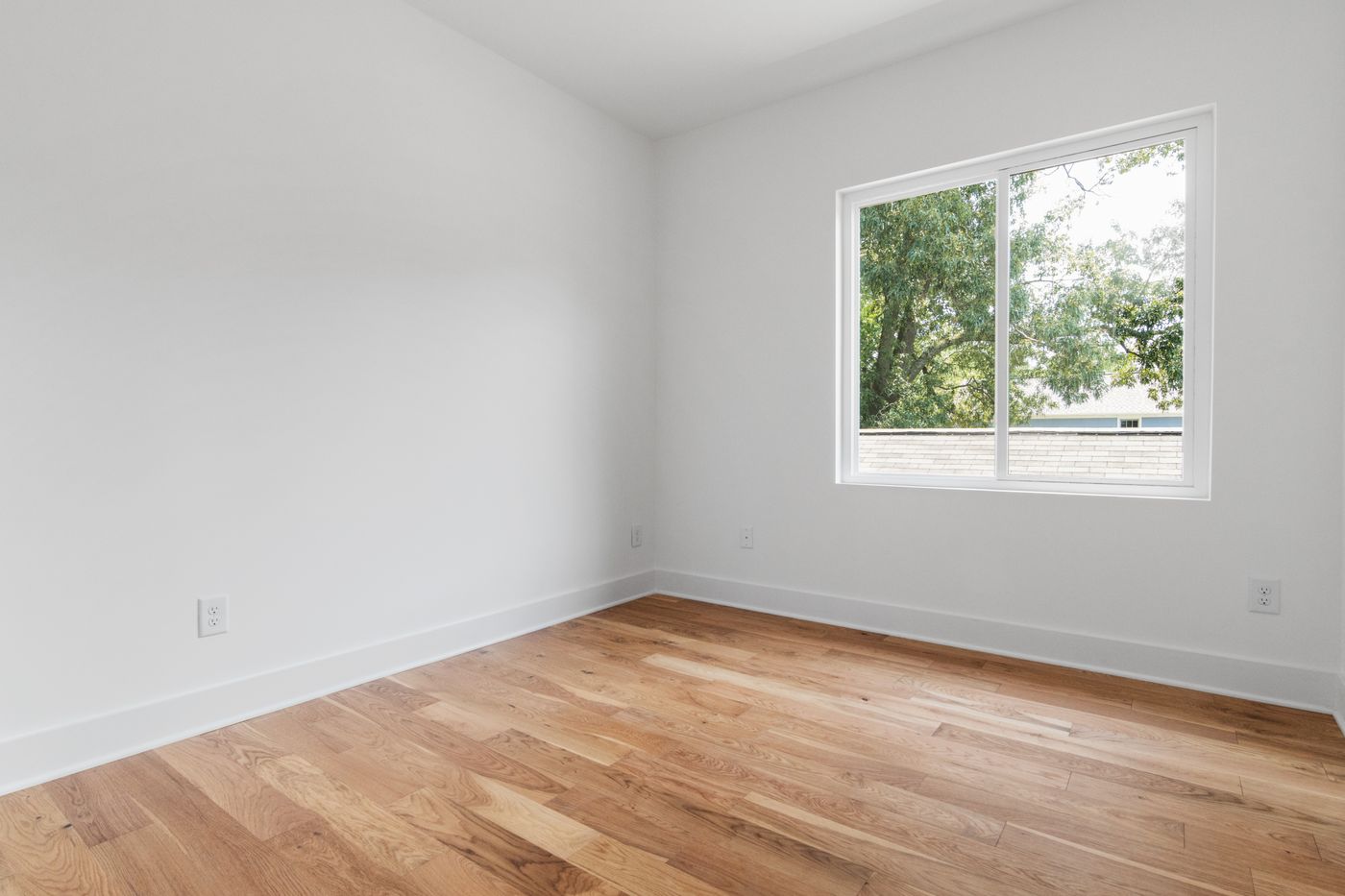 Habitación vacía con piso de madera y una ventana que da a las copas de los árboles