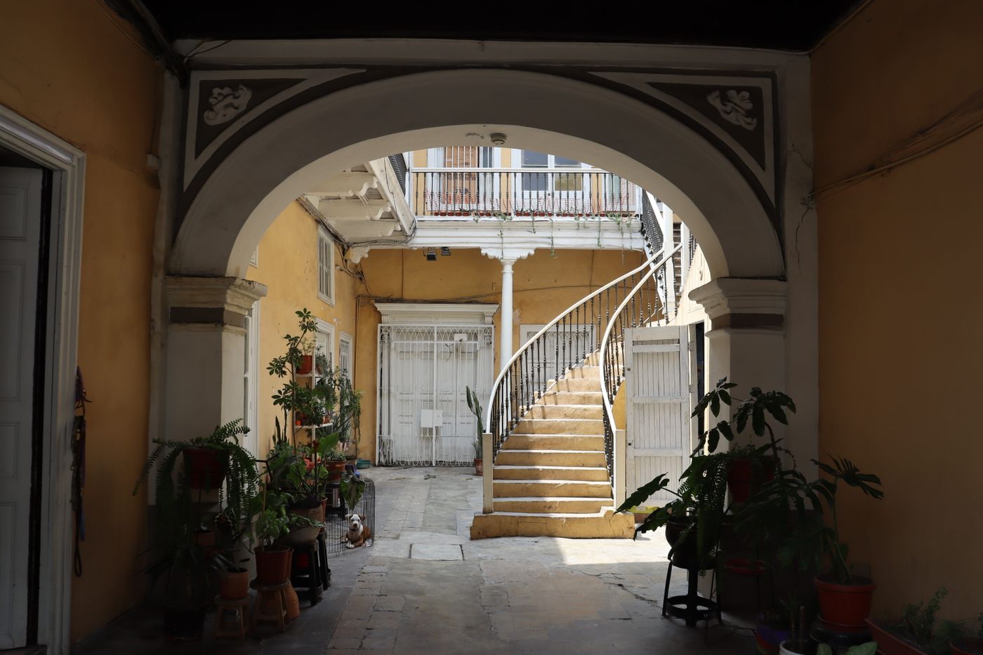 Patio interior de una casa antigua con arcos, escalera y plantas