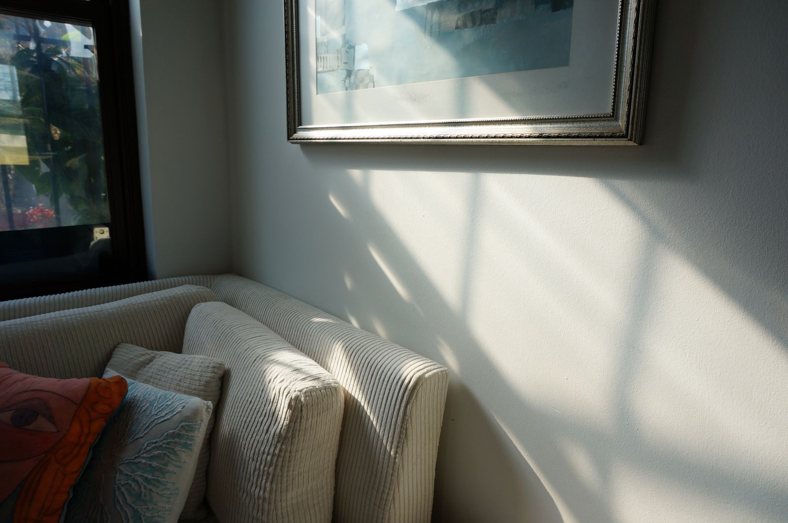 Sombra de una ventana dibujada por el sol sobre una pared blanca, junto a un sofá