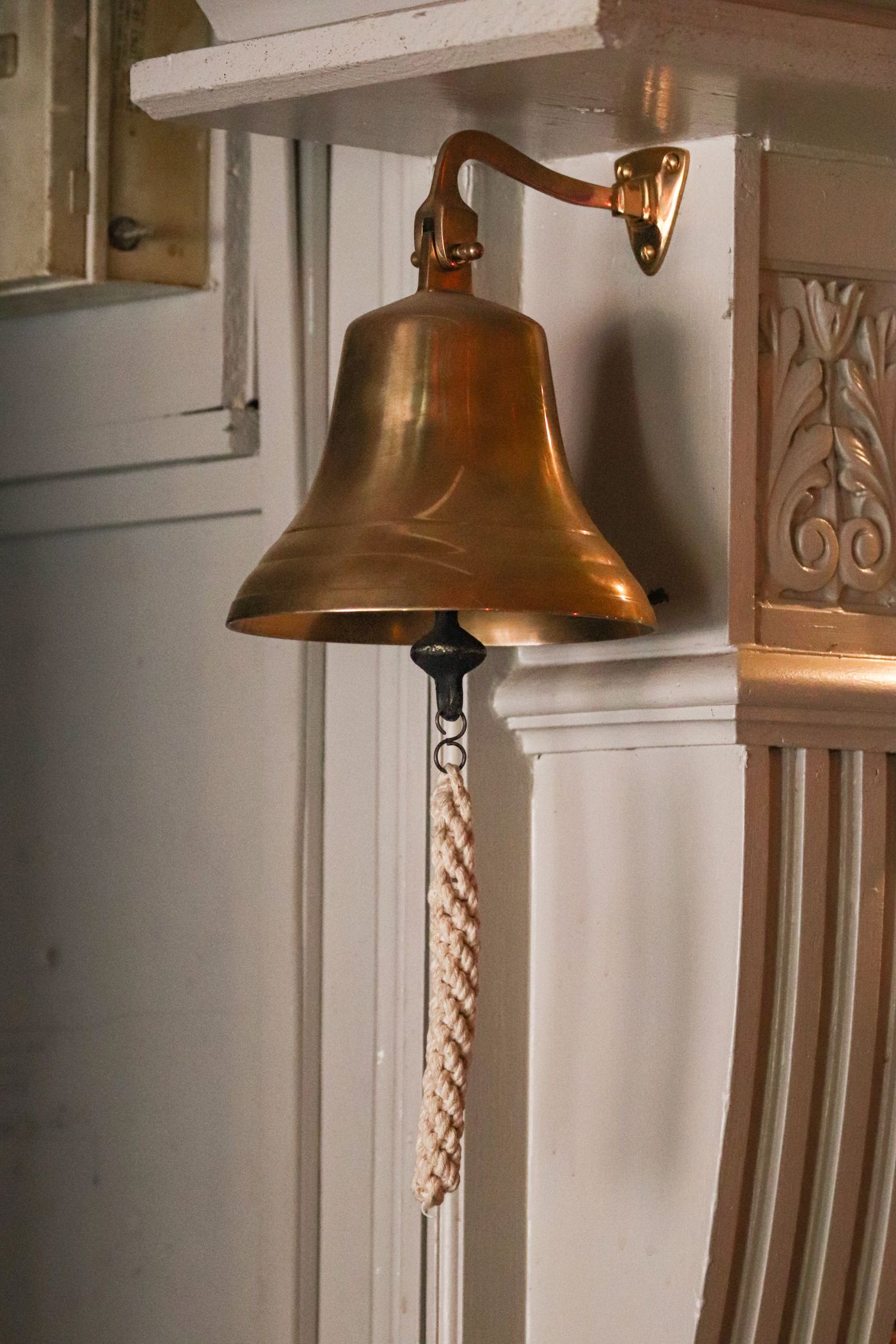 Una campana de bronce colgada de la pared, con su cuerda trenzada para tocarla