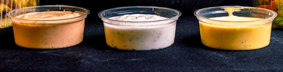 Tres taperitas de crema en fila: una rosada, una blanca y una amarilla