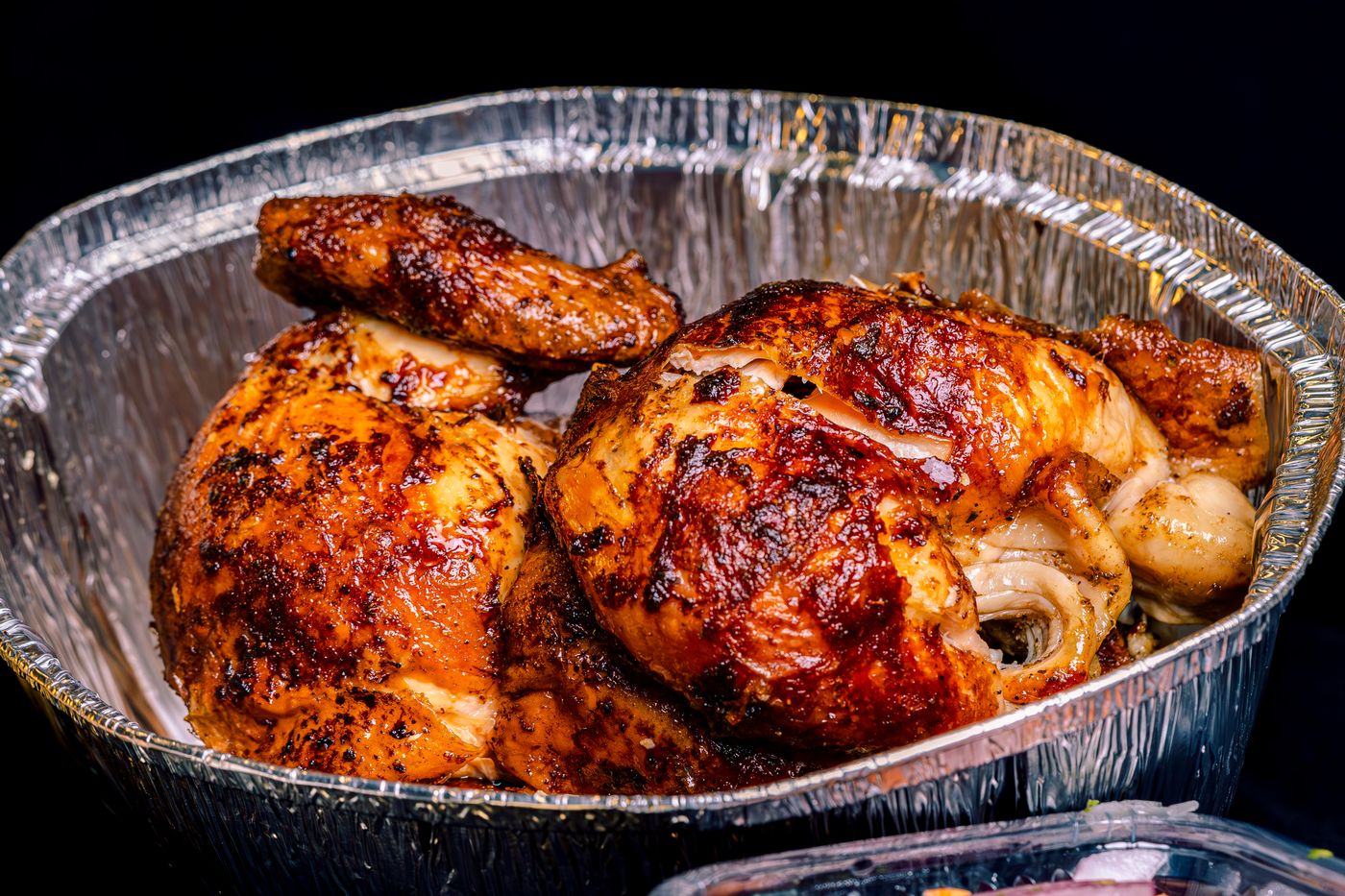 Pollo a la brasa dorado en su bandeja de aluminio, listo para el delivery