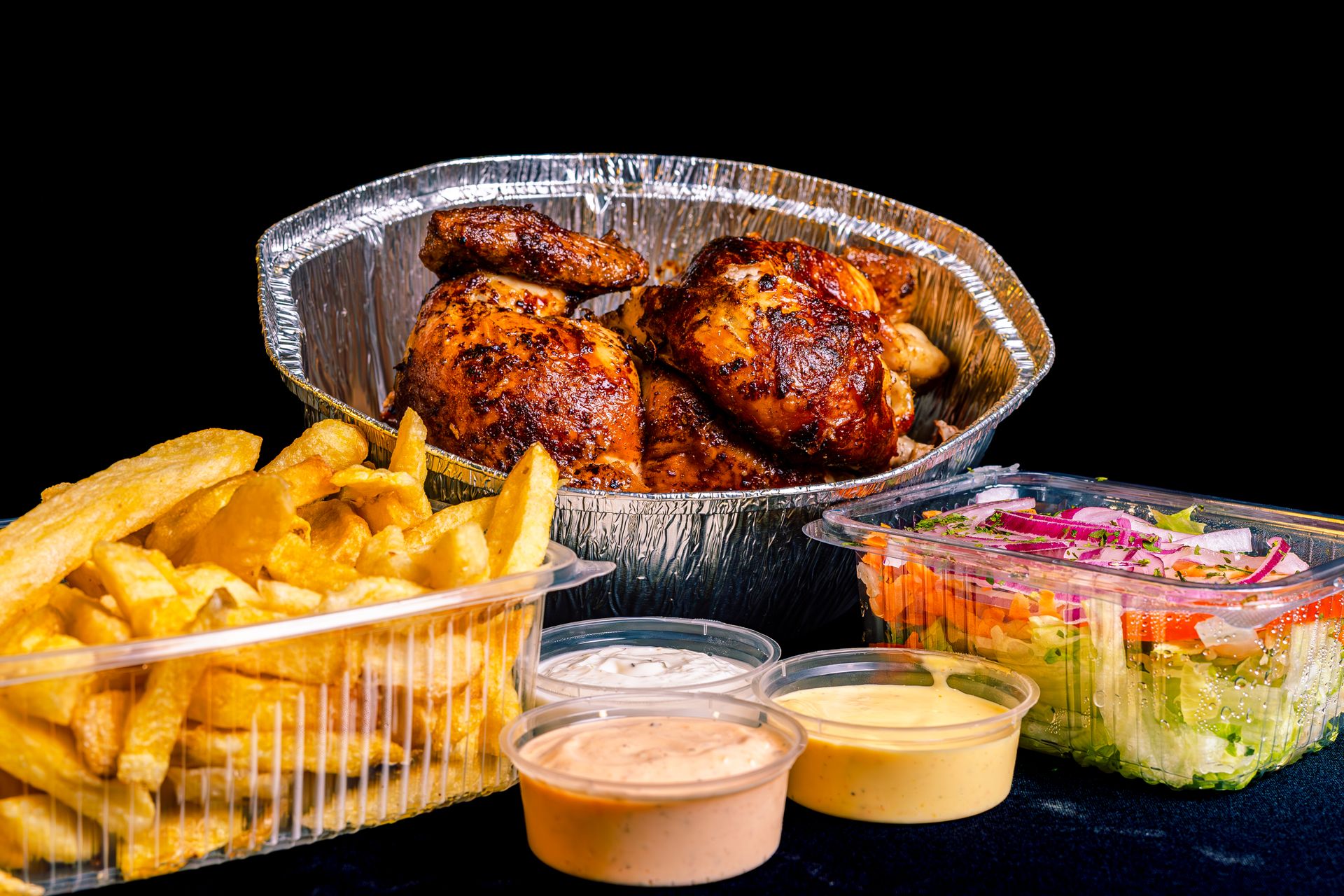 Pollo a la brasa en cuartos en su bandeja, con papas fritas, ensalada y tres cremas en taperitas